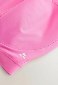 Felle roze sportshorts van zachte, rekbare stof. Heeft gebogen naden en een witte geometrische logo-accent in de onderste hoek.