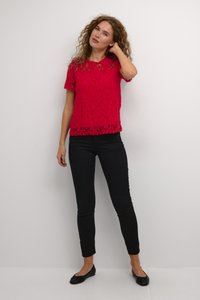 Haut en dentelle rouge à manches courtes et ourlet festonné, associé à un pantalon noir ajusté et des ballerines noires. Texture lisse, motif floral.
