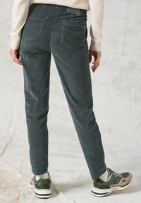 Grafitowe spodnie z korduroyu o slim fit, z dwoma tylnymi kieszeniami i subtelnymi detalami przeszyć; w połączeniu z zielono-beżowymi sneakersami.