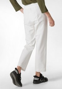 Pantalones cortos de algodón blanco con un corte relajado, cinturilla elástica y bolsillos laterales, combinados con zapatos deportivos negros con acentos en contraste.