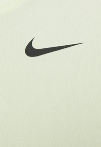 Vaaleanvihreä urheilukangas, jossa on sileä pinta ja jossa on keskeinen musta Nike-swoosh-logo. Muotoilu on minimalistinen ja moderni.