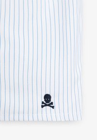 Tela blanca con rayas finas azules, que presenta un pequeño bordado negro de calavera y huesos cruzados cerca del dobladillo.