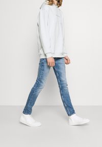 Ljusgrå bomullshoodie med framficka och dragsko, bärs tillsammans med medeltvättade slim fit jeans och vita högstövlar.