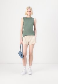 Grønn ermeløs topp, beige shorts, blå håndveske, hvite sneakers, stylet med hvite sokker. Antrekket er uformelt og lett.