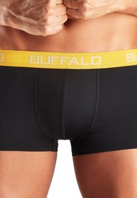 Melni bokseršorti ar dzeltenu elastīgu jostu, kurā balti ir izdrukāts vārds 'BUFFALO'. Gluda materiāla, pieguļoša dizaina un vidus līdz augšstilbam garuma.