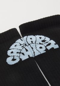 Chaussettes noires ornées d'un motif tricoté bleu clair avec des lettres audacieuses et arrondies. Le texte est centré en haut, avec une texture côtelée.