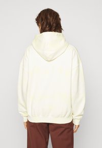 Sudadera con capucha en amarillo claro, que presenta un corte relajado, hombros caídos y puños y dobladillo acanalados. Textura suave con un patrón sutil.