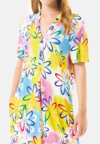 Vestido de manga corta hecho de una tela ligera, con un patrón floral multicolor sobre un fondo brillante amarillo y rosa, y con un cierre de botones en la parte delantera.