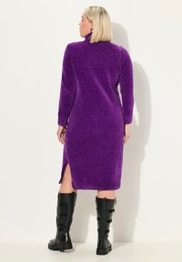 Abito lavorato a maglia viola con colletto alto, maniche lunghe, spacchi laterali e finitura testurizzata, abbinato a stivali neri al ginocchio con cinturini.
