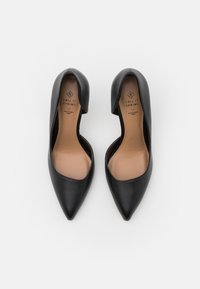 Chaussures noires à bout pointu avec une finition en cuir synthétique lisse. Présentent un design à encolure basse et un revêtement intérieur beige, étiqueté "végan durable".