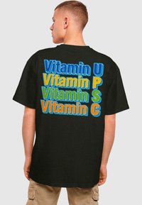 Svart T-skjorte med flerfargede bokstaver som sier "Vitamin U, P, S, C" i lekne skrifttyper. Korte ermer og avslappet passform.