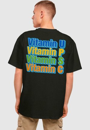 Black T-shirt featuring multicolored text stating "Vitamin U, P, S, C" in playful fonts. Short sleeves and a relaxed fit.