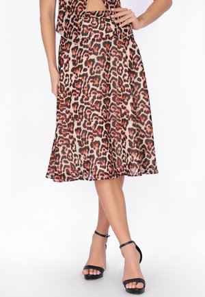 Kobieta ubrana w spódnicę o długości do kolan w nadruk w cętki lamparta oraz dopasowaną górę, zestawione z czarnymi sandałami na wysokim obcasie z paskiem wokół kostki.