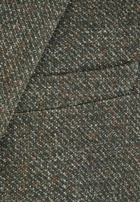 Close-up van een wollen tweed jaszak met een gestructureerd patroon in grijze, bruine en witte tinten.