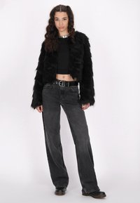 Zwarte nepbont jas met lange mouwen, gecombineerd met zwarte high-waisted, wijde jeans en zwarte klompen. Eenvoudige zilveren ketting als accent.