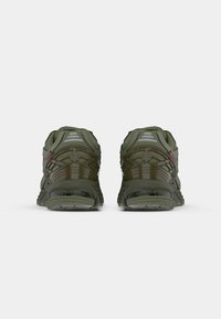 Baskets de sport vertes avec une tige en maille et synthétique, présentant des accents réfléchissants et une semelle en caoutchouc texturée. Vue arrière montrant les détails de conception.