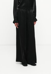 Čierne široké nohavice s textúrovaným leskom, majú elastický pás a voľný strih. Kombinované s textúrovanými čiernymi topánkami.