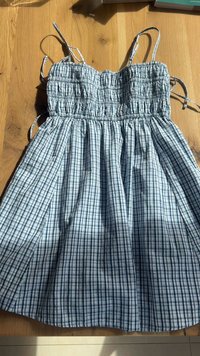 Vestido quadriculado azul e branco com corpete franzido, alças finas e saia plissada. Feito de tecido leve e apresenta um corte descontraído.