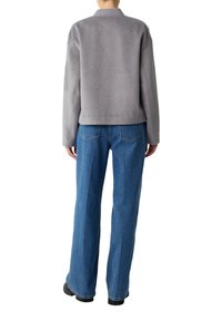 Graue Fleecejacke mit hohem Kragen, kombiniert mit hellblauen Weitenjeans. Das Outfit zeichnet sich durch schlichte Texturen und minimale Hardware-Details aus.