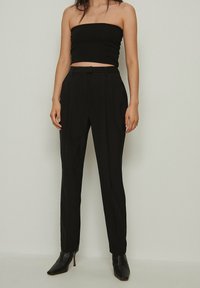 Black strapless top with ribbed texture paired with tailored black trousers. Trousers feature sharp pleats and are complemented by pointed black heels.