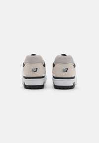 Egy pár fehér és szürke New Balance sportcipő hátulról, fekete logóval és texturált fekete talppal egy fehér háttér előtt.