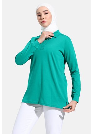 Langärmliges Polohemd in einfarbigem Teal, aus weichem Baumwollstoff gefertigt. Verfügt über einen klassischen Kragen, seitliche Schlitze und eine lockere Passform.