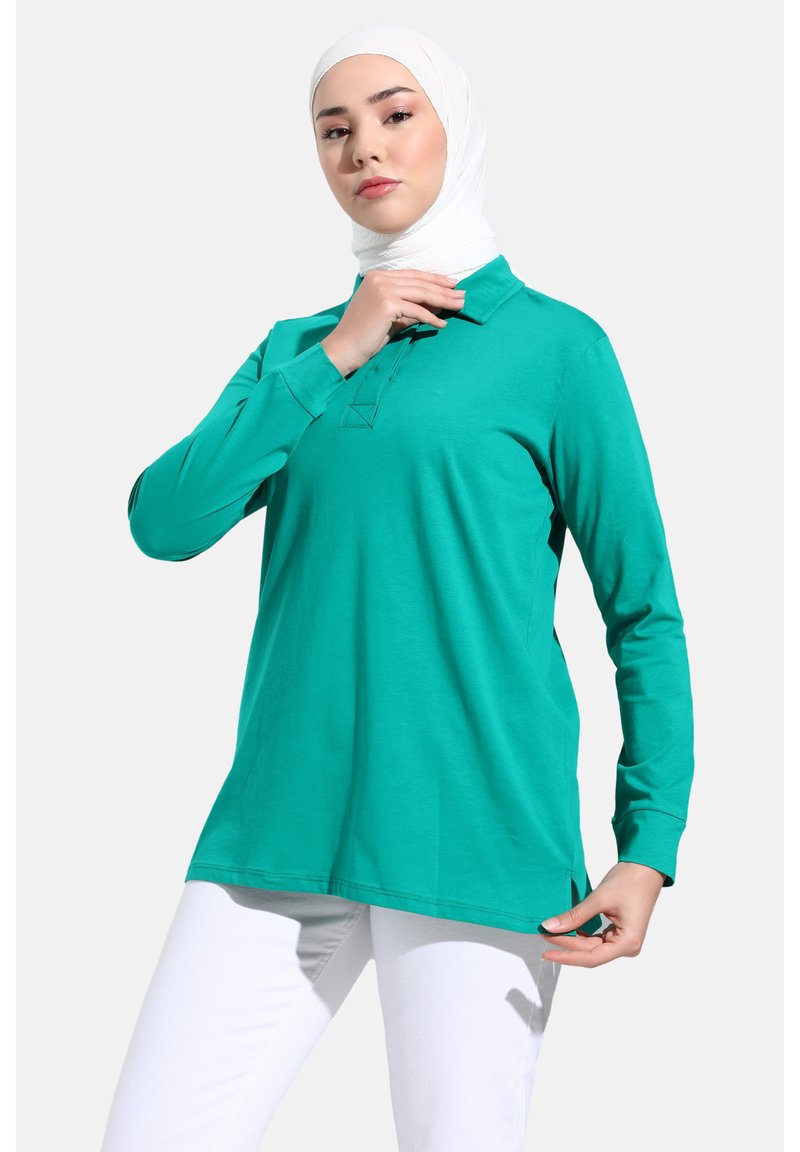 Polo a maniche lunghe di colore turchese, realizzato in morbido cotone. Caratterizzato da un colletto classico, fessure laterali e una vestibilità comoda.
