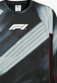 Schwarz-graues grafisches Sportoberteil mit F1-Logo, das diagonale Streifen, strukturierten Stoff und rote Akzente an der Schulternaht aufweist.