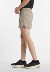 Beige patterned shorts with a split hem, featuring an elastic waistband and drawstring, paired with black athletic shoes.
