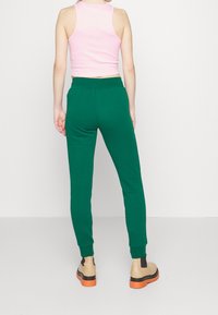 Gröna bomullsbyxor med elastisk midja och mudd, i kombination med en rosa linne och beige skor med orange sulor. Bakifrån.