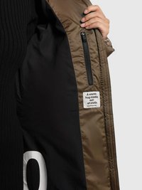 Kaki krāsas pūkains jaka iekšpuse ar melnu oderi, rāvējslēdzēja kabatu un etiķeti ar uzrakstu "Siltas apskāvienas no auduma."