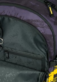 Zaino con una parte superiore viola e una parte inferiore nera e testurizzata. Presenta una tasca con zip e un marchio discreto all'interno.