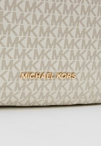 Beżowa torba Michael Kors z teksturowanym wzorem powtarzających się liter "K" oraz złotym logo. Gładka tkanina z akcentami.