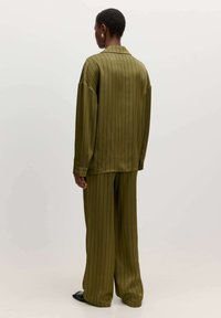 Olivgrünes, gestreiftes Oversized-Hemd und passende weite Hosen aus einem glatten Stoff. Bemerkenswerte Details sind die übergroßen Ärmel und Knöpfe.