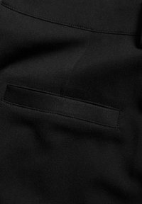 Svart tyg med en platt ficka med en slät yta. Sömdetaljerna är minimala och framhäver en elegant design.