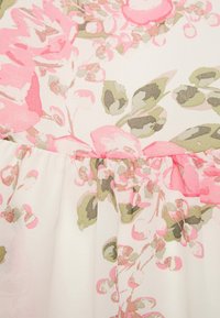 Tecido de vestido floral com grandes flores pink e verdes sobre um fundo branco; textura suave com detalhe de bainha franzida.