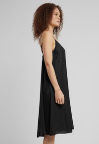 Svart, ärmlös klänning med tunna band, tillverkad av ett mjukt tyg. Flödande siluett som slutar precis ovanför knäet. Enkel, odekorerad design.