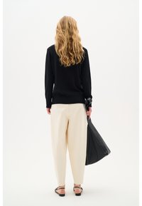 Maglione nero con orlo a coste, pantaloni larghi beige e una grande borsa in pelle nera. Visibili capelli lunghi e mossi e sandali piatti.