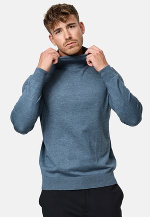 Suéter azul de punto con cuello alto, mangas largas y puños acanalados, que presenta una textura suave y un corte relajado.