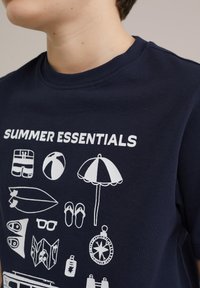 Marinblå bomullströja med vita grafiska illustrationer av sommarartiklar, inklusive en strandboll, parasoll och surfbräda.