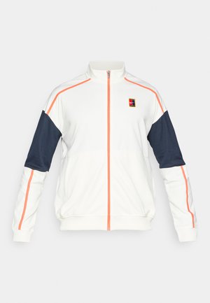 Bela športna zip-up jakna z mornarsko modrimi rokavi in oranžnimi detajli; ima visok ovratnik in logo na prsih. Gladka tekstura tkanine.