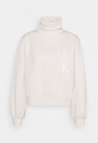 Krémový rolákový svetr s bílým logem Calvin Klein Jeans na přední straně a na rukávu, s žebrovanými manžetami a spodním lemem.