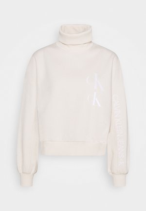 Krémový rolákový svetr s bílým logem Calvin Klein Jeans na přední straně a na rukávu, s žebrovanými manžetami a spodním lemem.