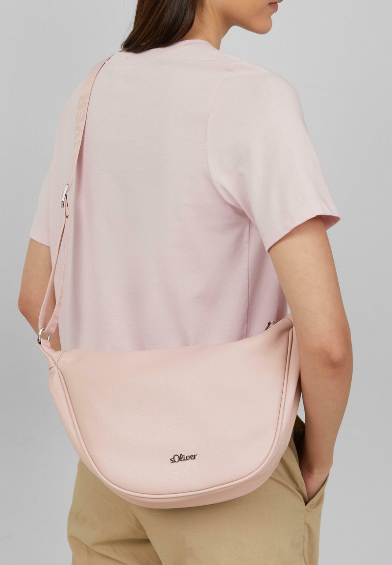 Różowa torba na ramię z sztucznej skóry o zaokrąglonym kształcie, z metalowymi elementami w kolorze srebrnym oraz wyszywanym logo. Regulowany pasek umożliwiający wszechstronne noszenie.