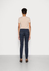 Marynarki w kolorze granatowym o dopasowanym kroju, z dwiema tylnymi kieszeniami zapinanymi na zamek oraz gładką, miękką fakturą. W połączeniu z jasnobeżową bluzką.