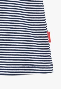 Marinblå och vitrandigt tyg med fina horisontella linjer. Har en röd etikett på sidan och en fållad kant som tillför textur och detalj.