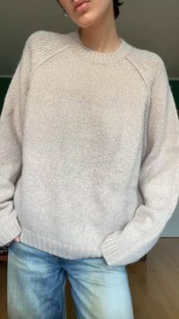 Helle beige Strickpullover mit Rundhalsausschnitt und gerippten Bündchen, der eine lockere Passform und weiche Textur aufweist, kombiniert mit blauen Jeans.