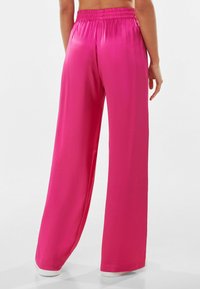 Pink satin wide-leg pants with an elastic waistband, smooth texture, and a flowing silhouette to the floor, showcasing a vibrant hue.