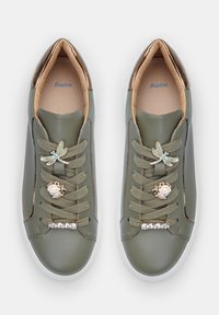 Green leather sneakers with bronze accents, featuring decorative lace embellishments: dragonfly and two gems, textured laces, and white soles.