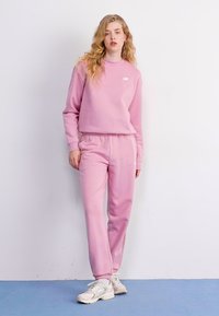 Sweatshirt rose et pantalon de survêtement assorti en tissu doux, avec un design ajusté et un petit logo sur la partie supérieure gauche de la poitrine.